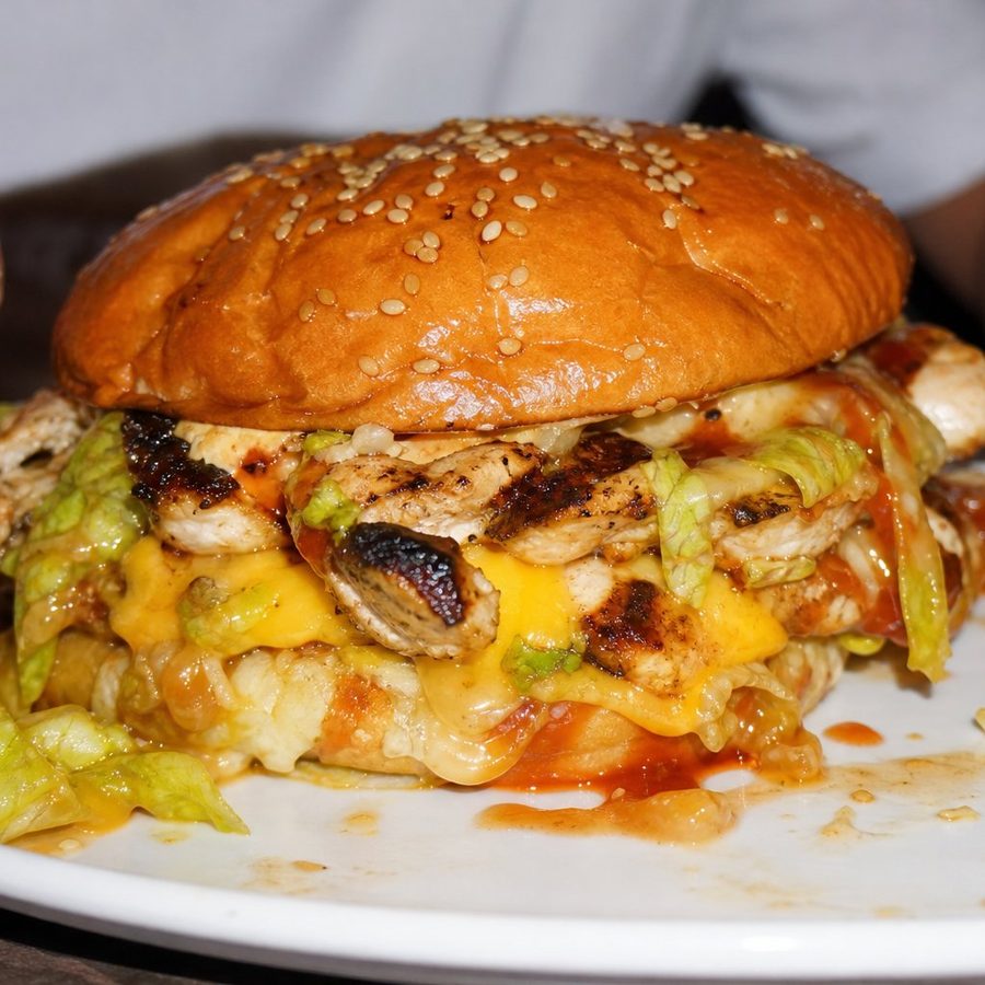 A grilled chicken burger in a sesame bun, packed with salad and sauce