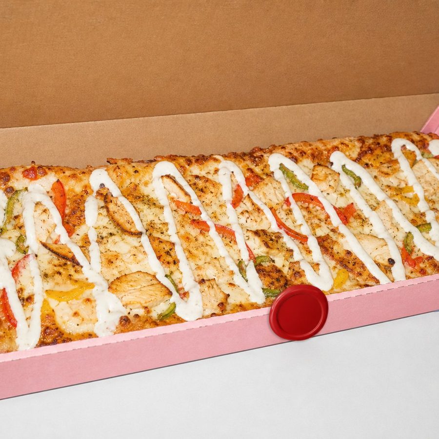 A long rectangular Long Shots pizza in its pink box with a white sauce drizzle