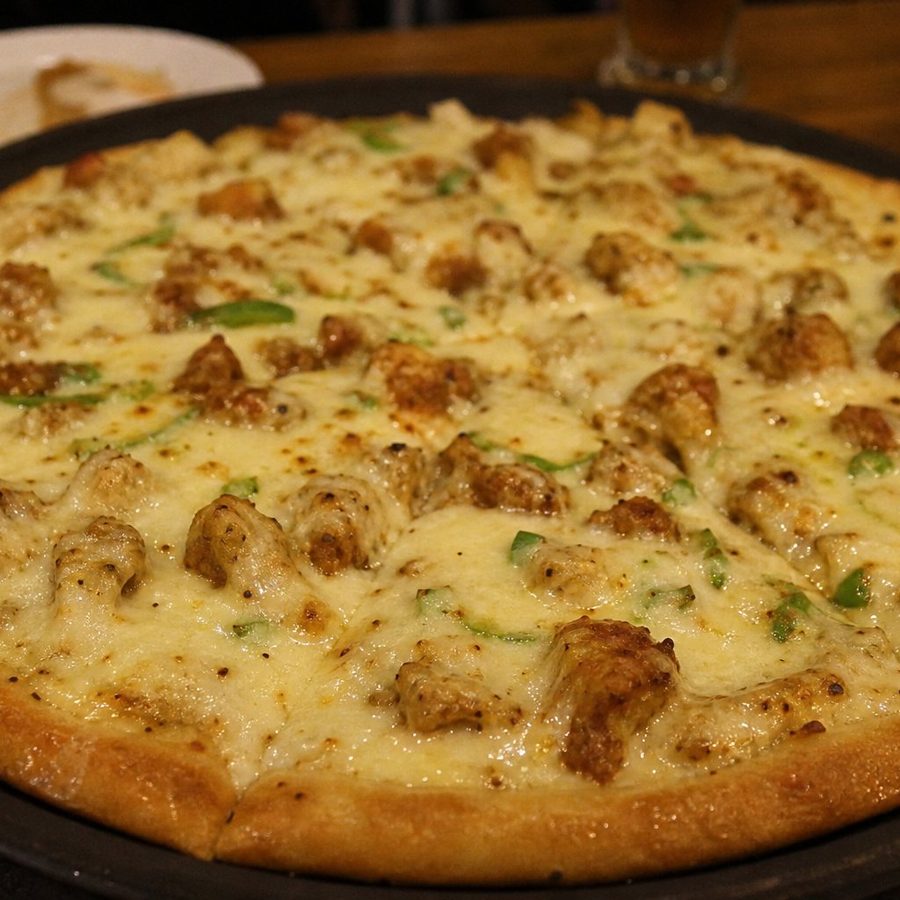 A Malai Boti pizza on a black pan, creamy white chicken pieces across melted cheese