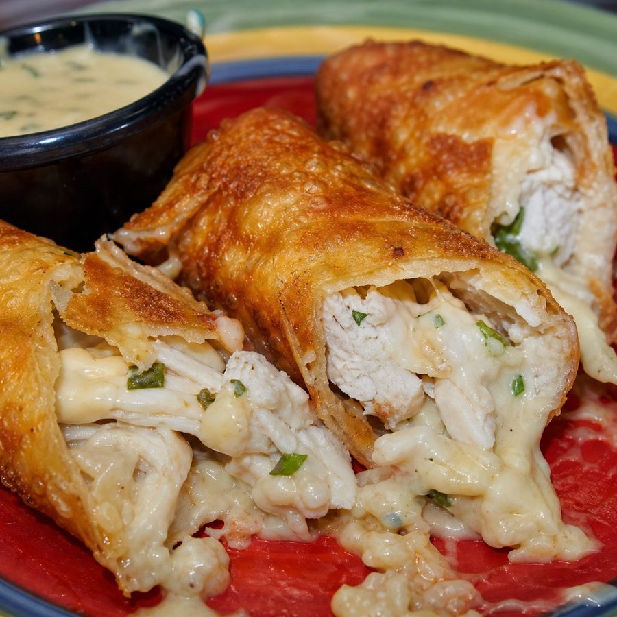 Creamy chicken spin rolls cut open beside a pot of dip